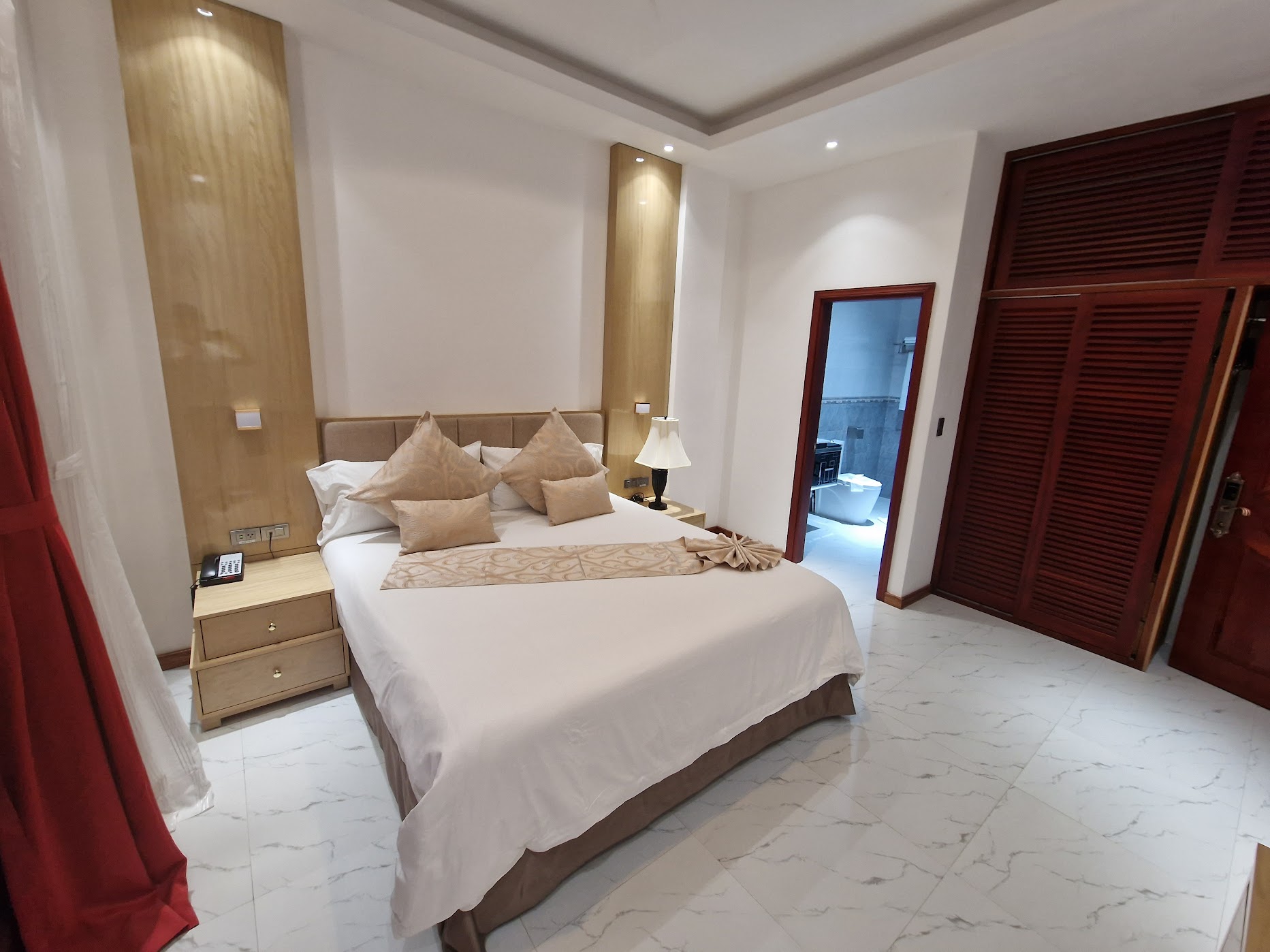 King bed with warm-toned wood panelling and en-suite bathroom at L'ver Hotel, Somoto